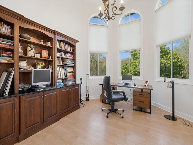 home office with an inviting chandelier, light wood-style flooring, baseboards, and a towering ceiling