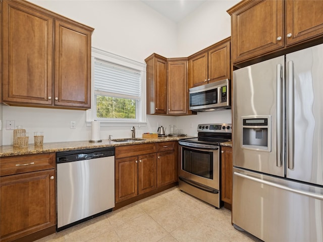 kitchen with a sink, light stone counters, stainless steel appliances, and brown cabinets