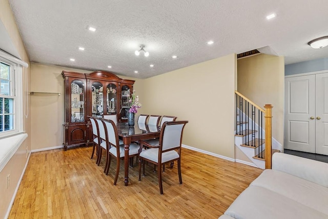 dining space featuring light wood-style floors, baseboards, stairway, and a textured ceiling