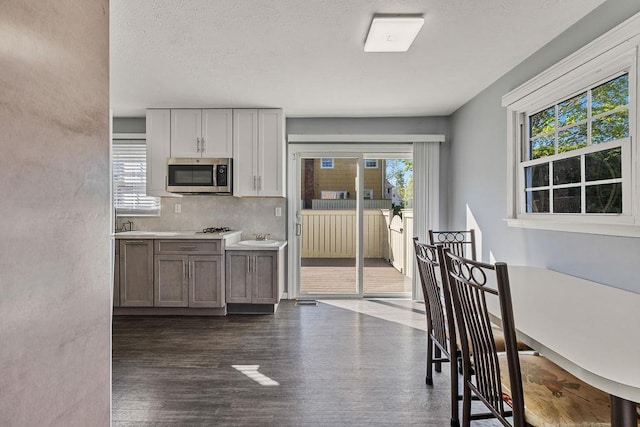 kitchen featuring a sink, light countertops, stainless steel microwave, tasteful backsplash, and dark wood-type flooring