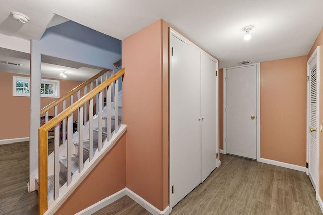 corridor with baseboards, wood finished floors, visible vents, and stairway