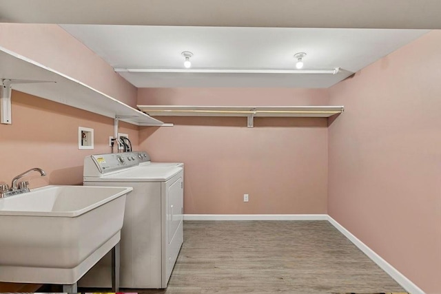 washroom with laundry area, light wood-type flooring, a sink, baseboards, and washer and clothes dryer