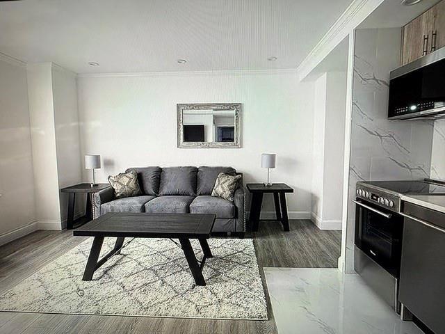 living area with crown molding, baseboards, and light wood-style floors