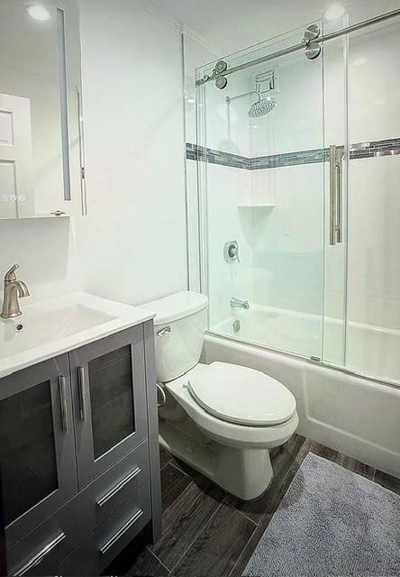 150 W 51 Unit 1032, New York Manhattan, NY 10019 - bathroom featuring bath / shower combo with glass door, toilet, vanity, and wood tiled floors