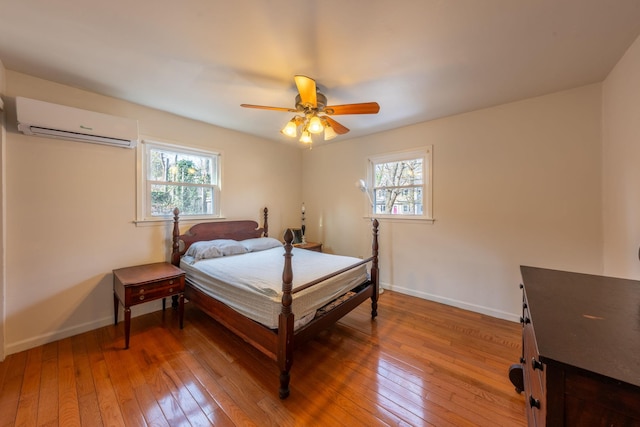 bedroom featuring baseboards, a wall unit AC, multiple windows, and light wood-type flooring