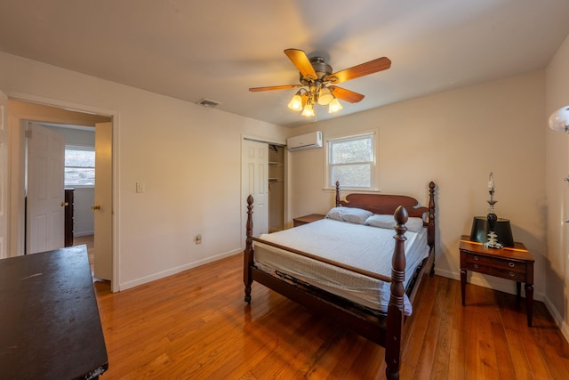 bedroom with an AC wall unit, light wood finished floors, and multiple windows