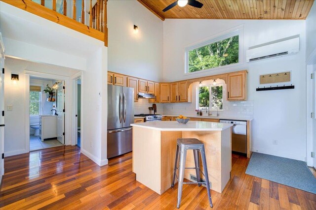kitchen featuring appliances with stainless steel finishes, a center island, a wall mounted air conditioner, wooden ceiling, and under cabinet range hood