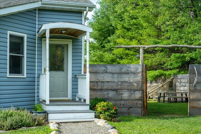 doorway to property featuring fence and a shingled roof