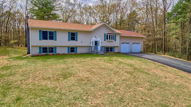 raised ranch with an attached garage, aphalt driveway, and a front yard