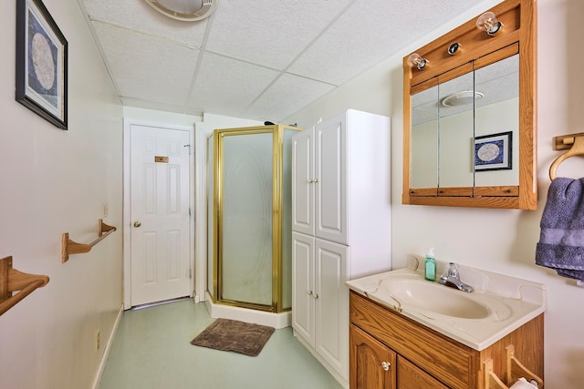 bathroom with baseboards, a shower stall, a paneled ceiling, and vanity