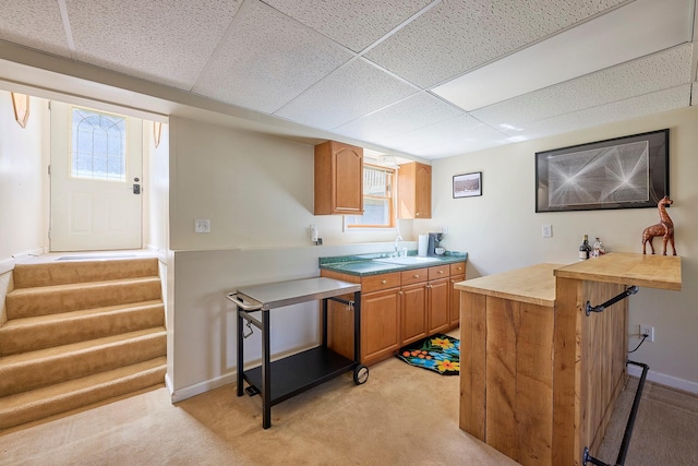 kitchen featuring a paneled ceiling, light colored carpet, a sink, baseboards, and wood counters