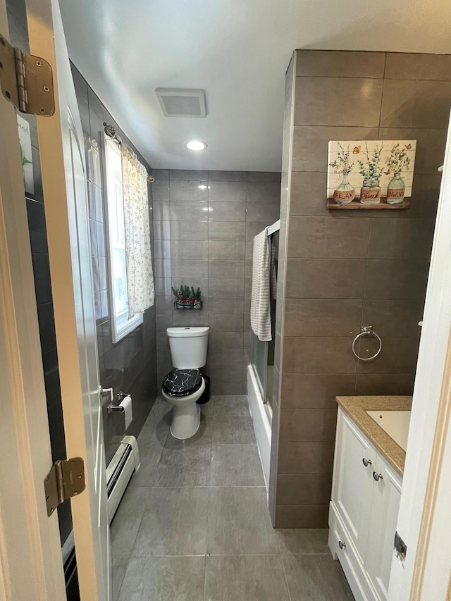 58 7th St, Valley Stream, NY 11581 - bathroom with tile walls, baseboard heating, vanity, tile patterned floors, and bath / shower combo with glass door