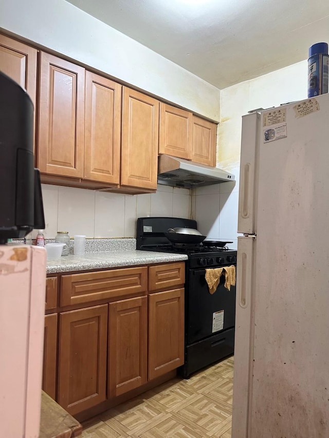 kitchen featuring freestanding refrigerator, black gas stove, light countertops, under cabinet range hood, and brown cabinets