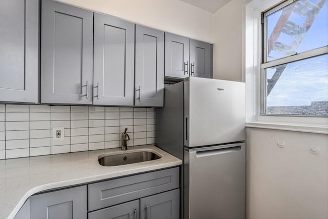 kitchen featuring light stone counters, a sink, gray cabinets, freestanding refrigerator, and tasteful backsplash