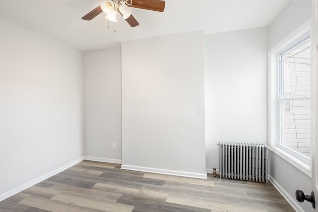 spare room featuring radiator heating unit, plenty of natural light, a ceiling fan, and wood finished floors