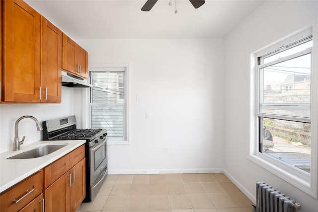 kitchen with a ceiling fan, stainless steel range with gas stovetop, a sink, radiator heating unit, and under cabinet range hood