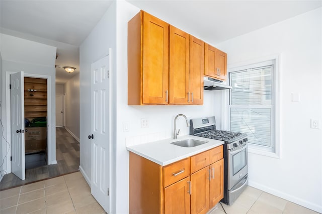 kitchen featuring gas range, light countertops, under cabinet range hood, a sink, and light tile patterned floors