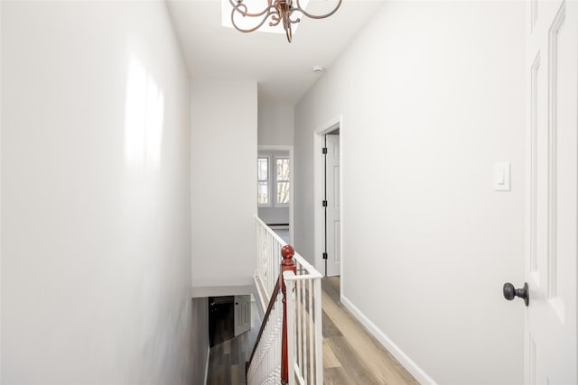 corridor featuring a notable chandelier, an upstairs landing, baseboards, and light wood-type flooring