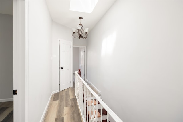 hallway featuring light wood-style floors, a skylight, baseboards, an upstairs landing, and an inviting chandelier