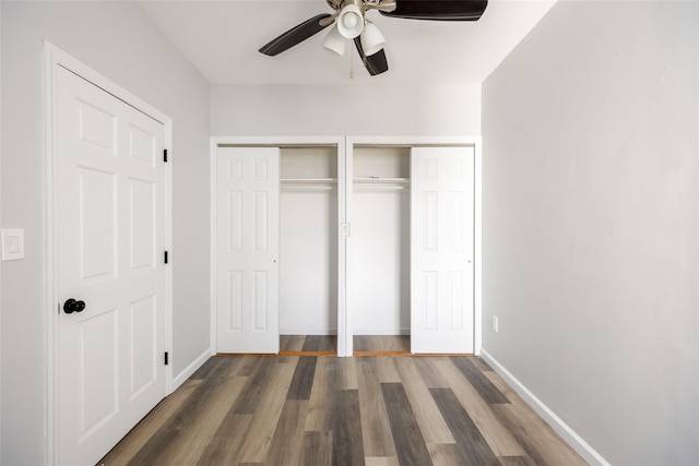 unfurnished bedroom with two closets, baseboards, ceiling fan, and wood finished floors