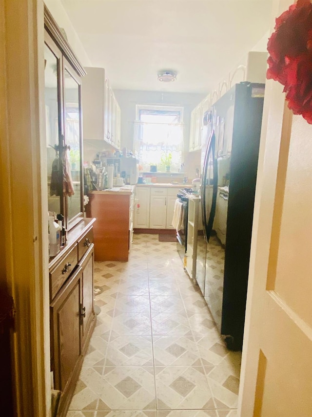 kitchen with freestanding refrigerator, range, white cabinets, and light countertops