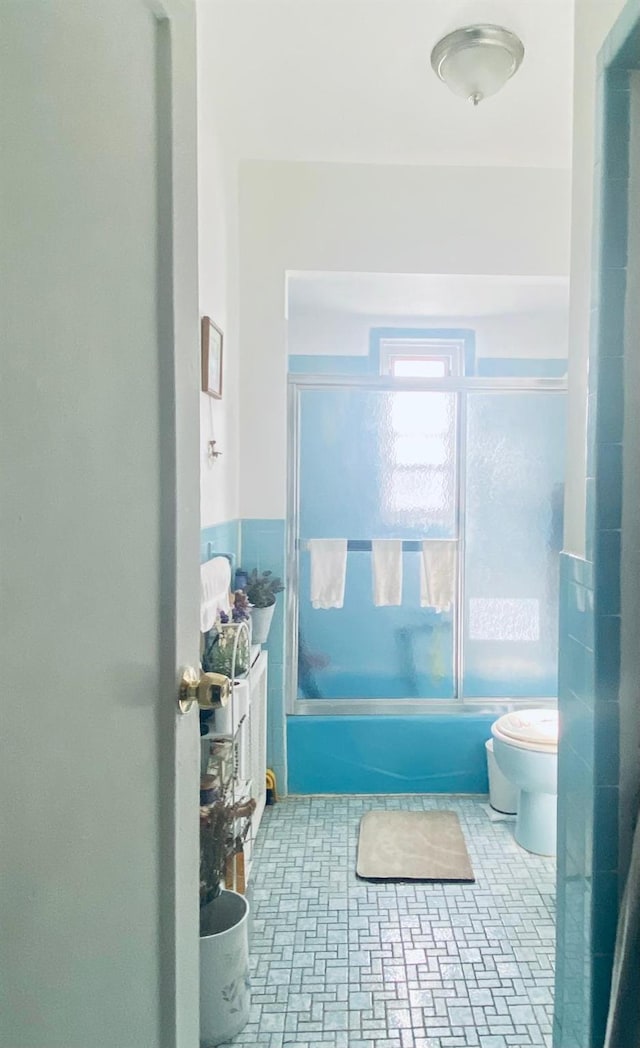 full bath featuring combined bath / shower with glass door and toilet