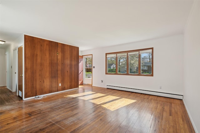 empty room with baseboards, wood-type flooring, and a baseboard heating unit