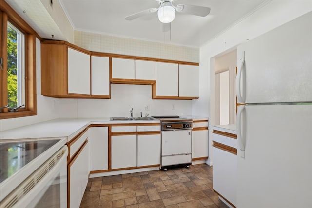 kitchen with white appliances, light countertops, white cabinetry, a sink, and stone finish flooring