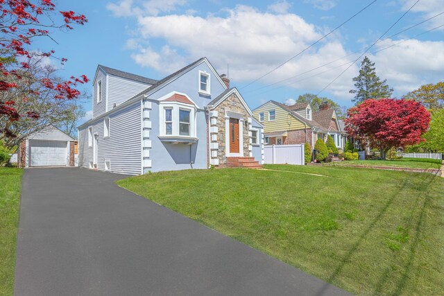view of front of property featuring a front yard, an outbuilding, a garage, fence, and aphalt driveway