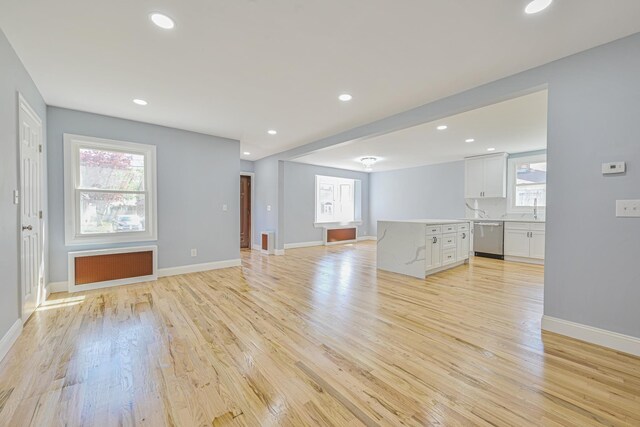 unfurnished living room with a sink, light wood-style flooring, radiator, and baseboards