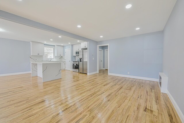 unfurnished living room with light wood-style floors, baseboards, recessed lighting, and a sink