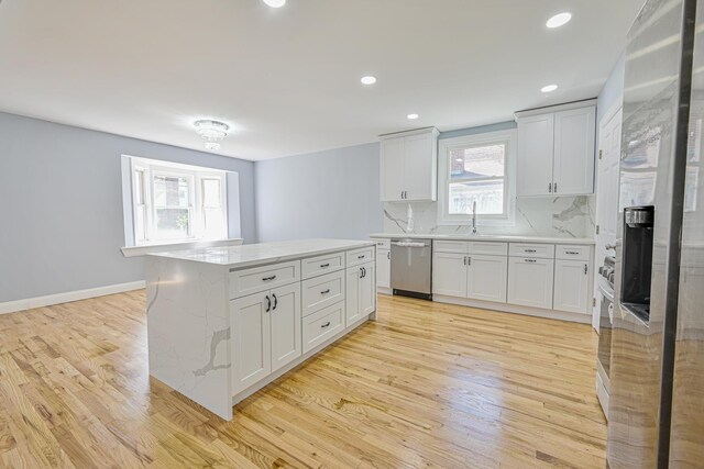 kitchen featuring stainless steel dishwasher, a sink, light wood finished floors, and a wealth of natural light