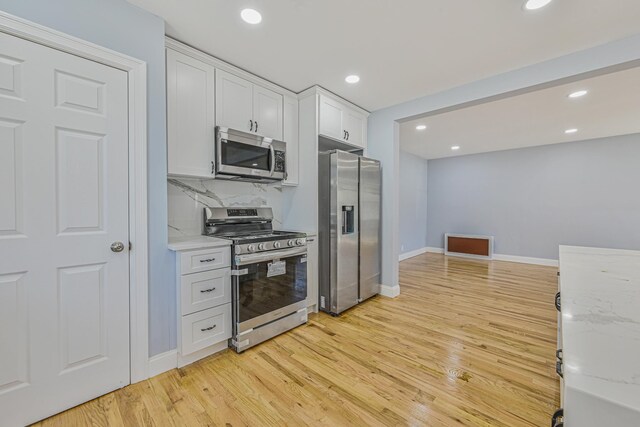 kitchen with light stone countertops, light wood-style floors, baseboards, white cabinets, and appliances with stainless steel finishes