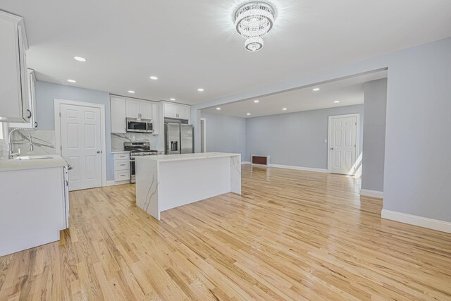 kitchen with a sink, light wood-style floors, a center island, stainless steel appliances, and baseboards