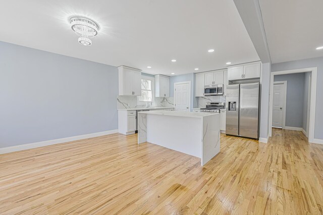 kitchen with backsplash, light countertops, baseboards, stainless steel appliances, and light wood-style flooring