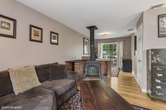 living room featuring baseboards, visible vents, wood finished floors, and a wood stove