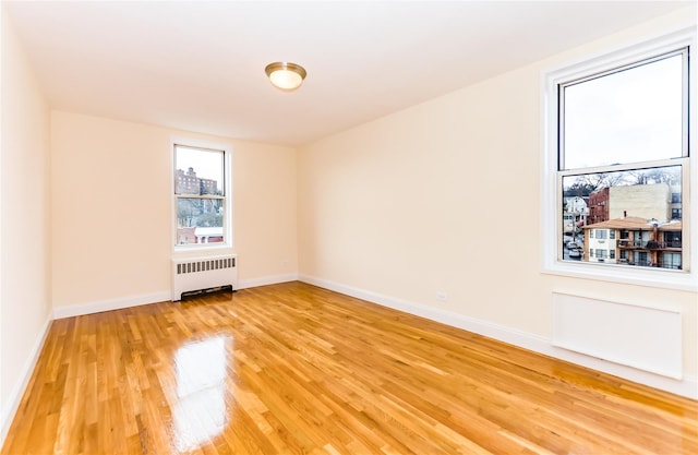 spare room with radiator heating unit, light wood-style floors, and baseboards