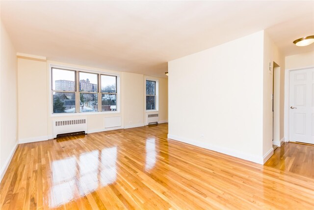 empty room with radiator heating unit, light wood-style floors, and baseboards
