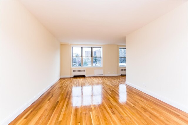 empty room with radiator, light wood-style floors, and baseboards