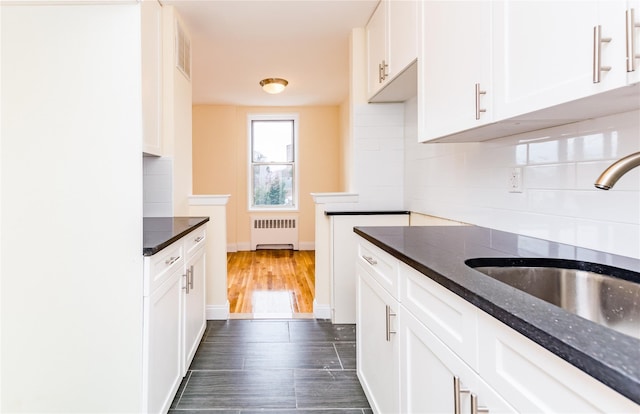 kitchen with radiator, a sink, dark wood-style floors, white cabinetry, and backsplash