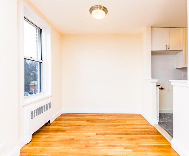 unfurnished dining area featuring radiator, light wood finished floors, and baseboards