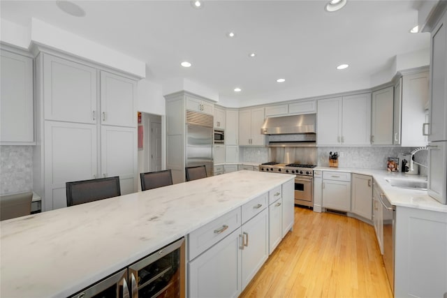 kitchen with a sink, built in appliances, gray cabinets, light wood-style flooring, and under cabinet range hood