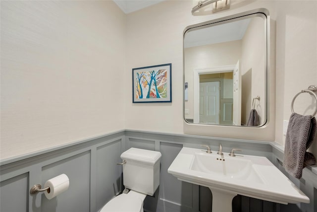 half bathroom with toilet, wainscoting, a sink, and a decorative wall