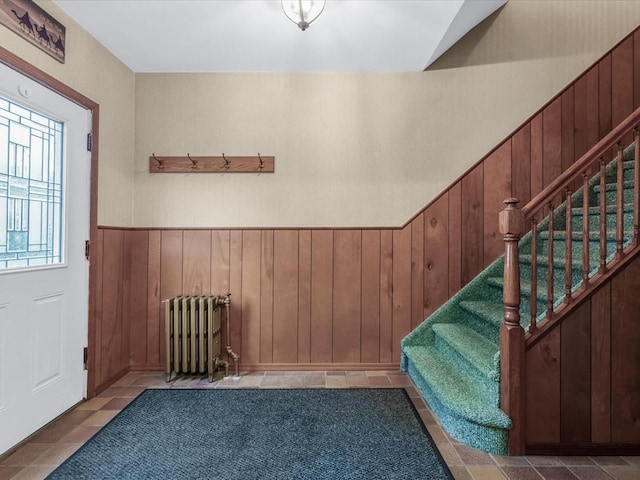 foyer featuring radiator, stairway, a wainscoted wall, and wooden walls