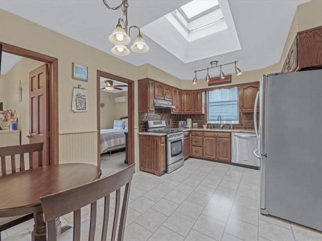 kitchen with appliances with stainless steel finishes, under cabinet range hood, a sink, a skylight, and light countertops