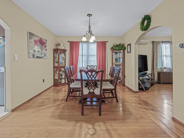 dining room featuring a wall mounted air conditioner, arched walkways, light wood-style flooring, a chandelier, and radiator