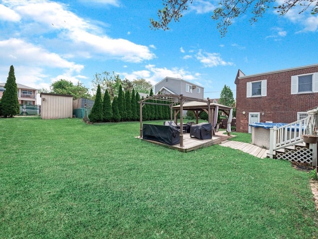 view of grassy yard featuring a gazebo, a deck, a storage unit, and an outbuilding