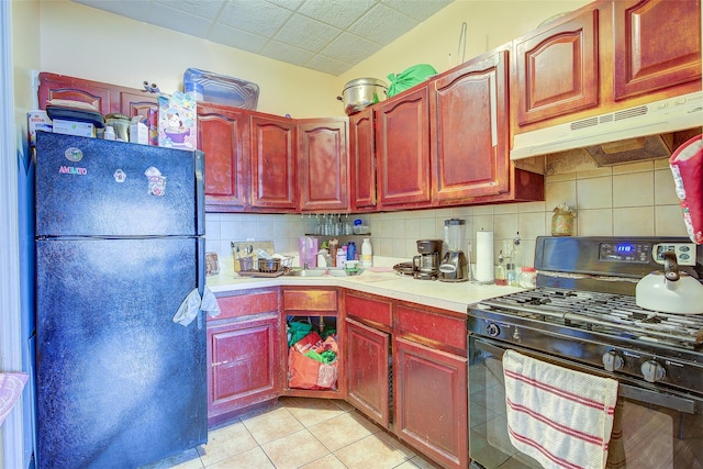 kitchen with light countertops, decorative backsplash, reddish brown cabinets, under cabinet range hood, and black appliances