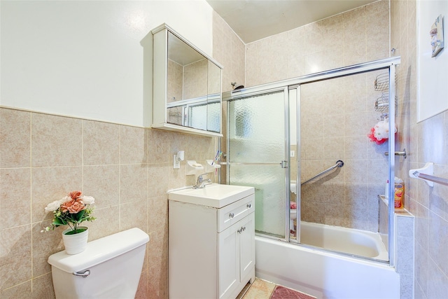 full bath with vanity, tile walls, combined bath / shower with glass door, and toilet