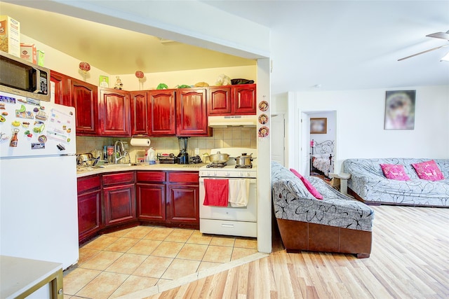 kitchen featuring backsplash, light countertops, reddish brown cabinets, under cabinet range hood, and white appliances
